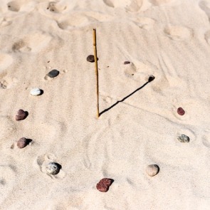 DIY sundial in the sand with shells and a stick