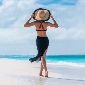 woman wearing swimsuit cover up and hat walking on the beach | Plumlee Gulf Beach Realty