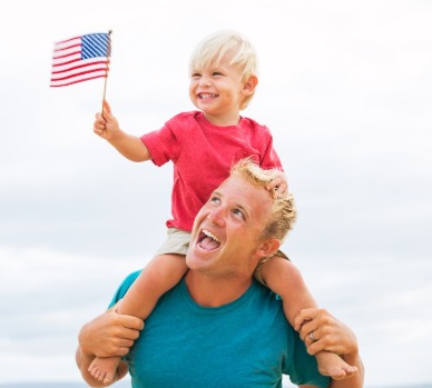 Little boy on Dad's shoulders waving American flag at the beach | Plumlee Indian Rocks Beach Rentals