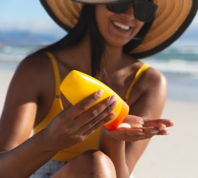 Woman wearing sun hat applying sunscreen on beach | Plumlee Indian Rocks Beach rentals